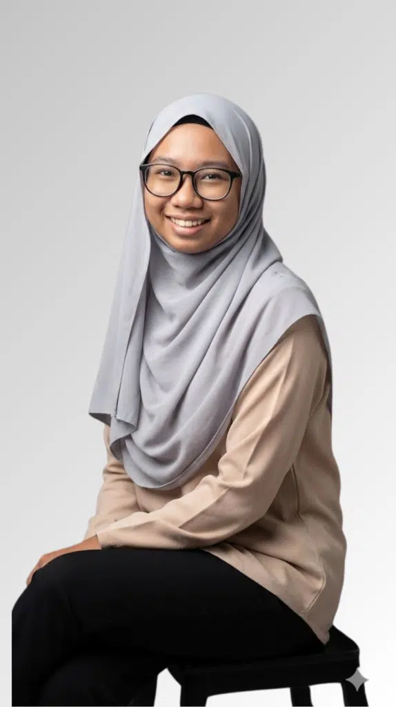 A woman in glasses and a light gray hijab smiles while seated on a stool against a plain gray background, promoting Sec 3 (2026) Pure Physics (Monday 8:30pm - 10:00pm).