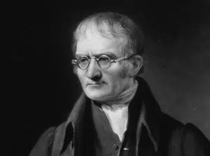 A black-and-white portrait of an older man with glasses, short hair, and formal 19th-century attire, looking slightly to the side.