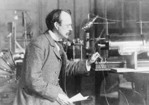A man in a suit operates scientific equipment in a laboratory, adjusting controls next to a glass tube apparatus on a table.