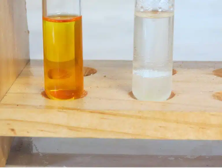 Two test tubes in a wooden rack: one holds an orange liquid, while the other contains a clear liquid with white precipitate at the bottom—demonstrating reactions between different functional groups.