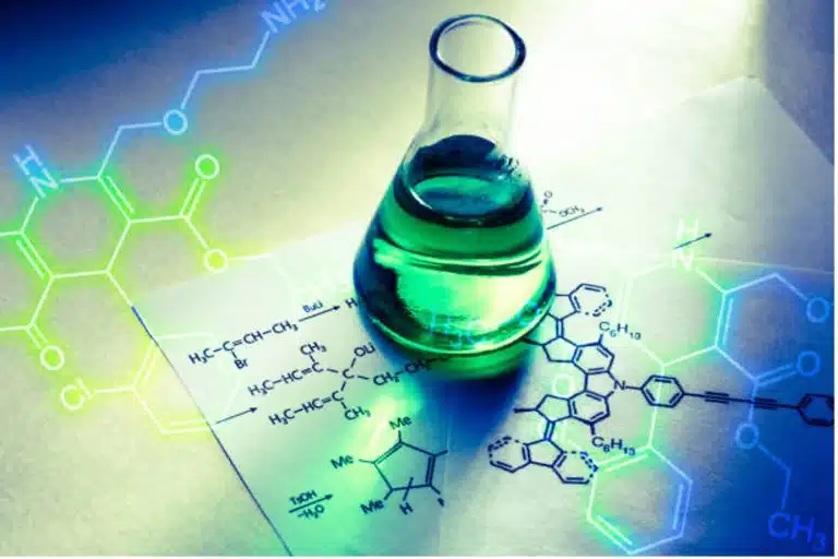 A glass flask filled with green liquid sits on papers displaying chemical structures, functional groups, and formulas, illuminated by bright, colorful light.