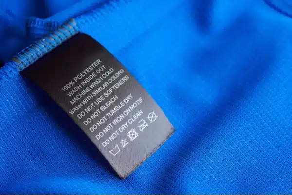 Black garment care label on bright blue fabric shows washing instructions and fabric composition: 100% polyester, a result of polymerisation. Machine wash cold; do not bleach, tumble dry, or dry clean.
