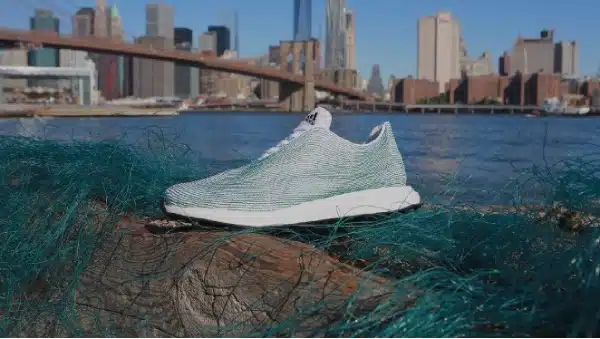 A sneaker made through polymerisation from recycled materials sits on a log covered in green netting, with a city skyline and bridge in the background.